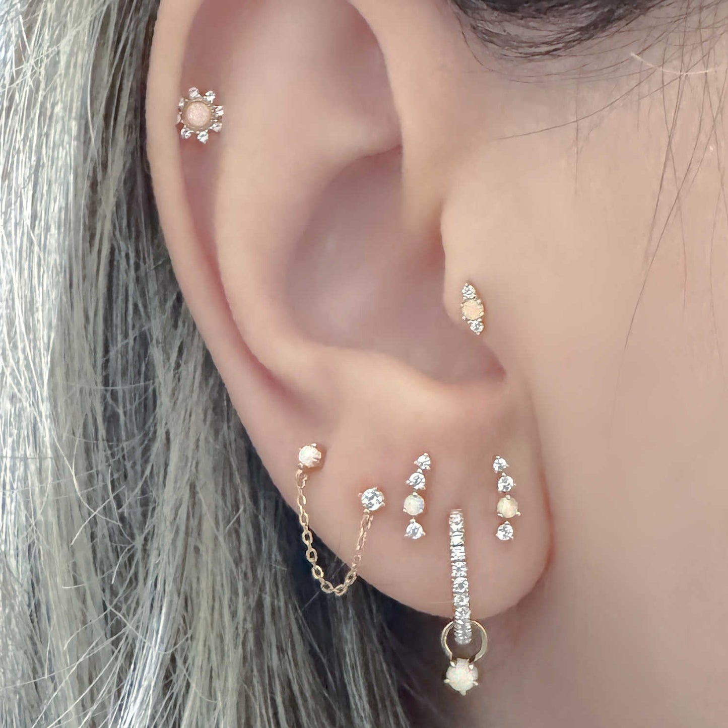 Close-up of a woman's ear with multiple diamond and opal earrings - hoops, studs, helix, tragus, and double piercing