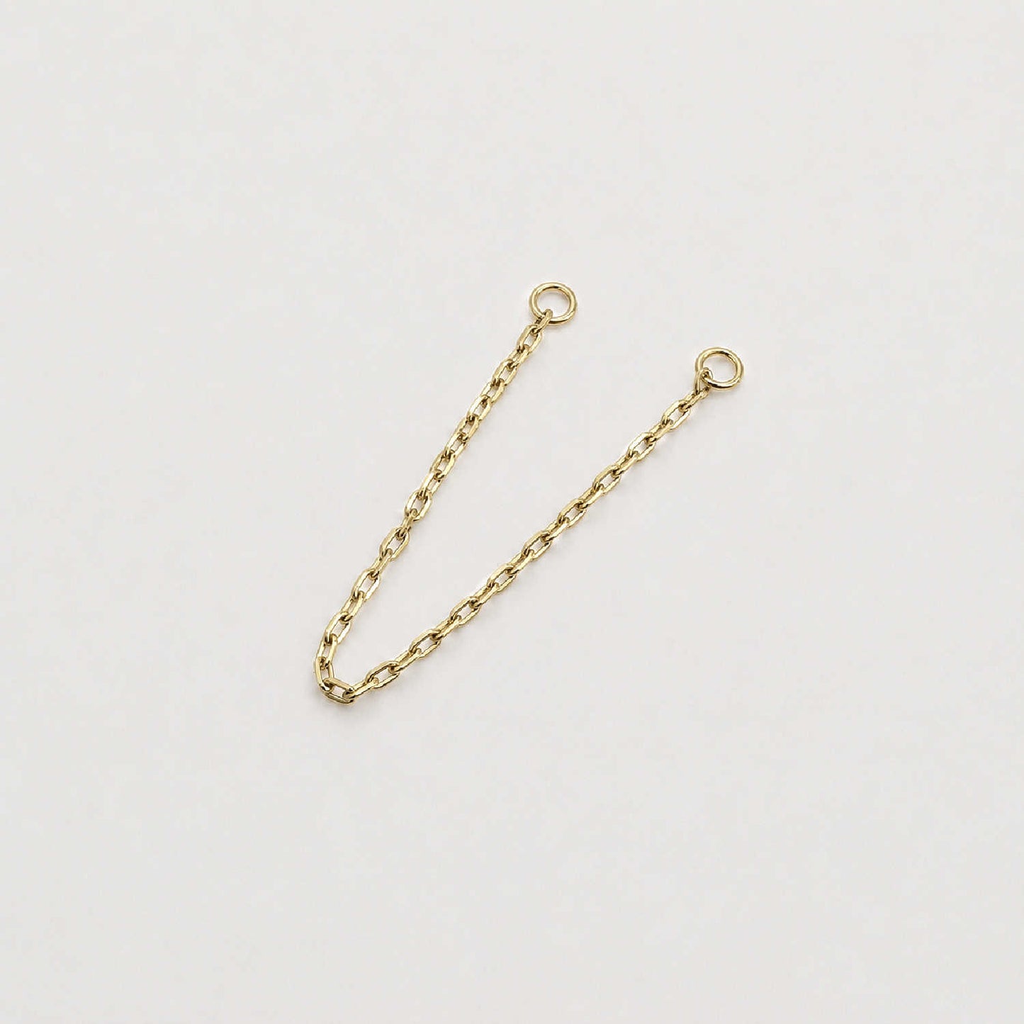 A 14k yellow gold cable chain double piercing earring charm with two circular jump ring ends, photographed on a plain light background.