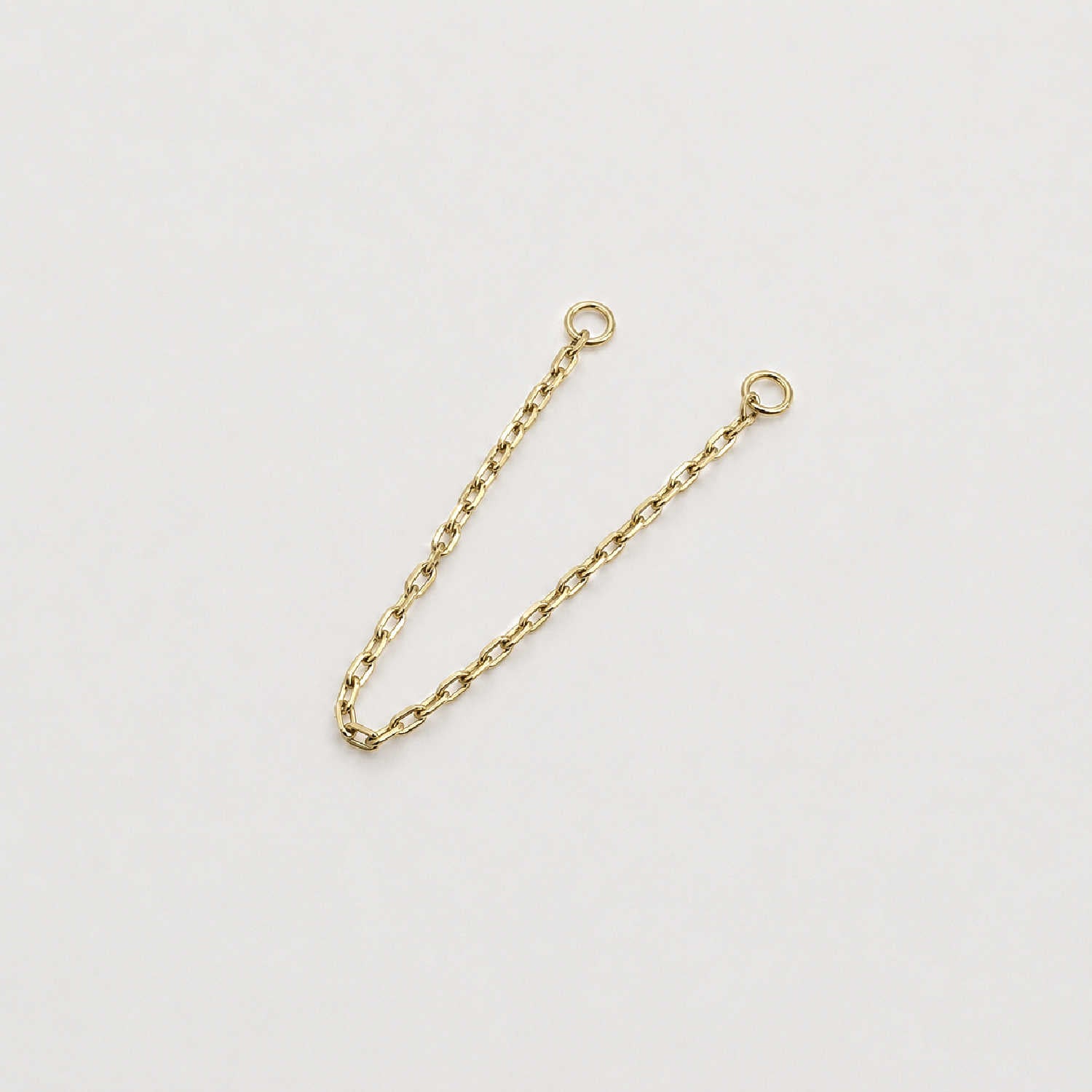 A 14k yellow gold cable chain double piercing earring charm with two circular jump ring ends, photographed on a plain light background.