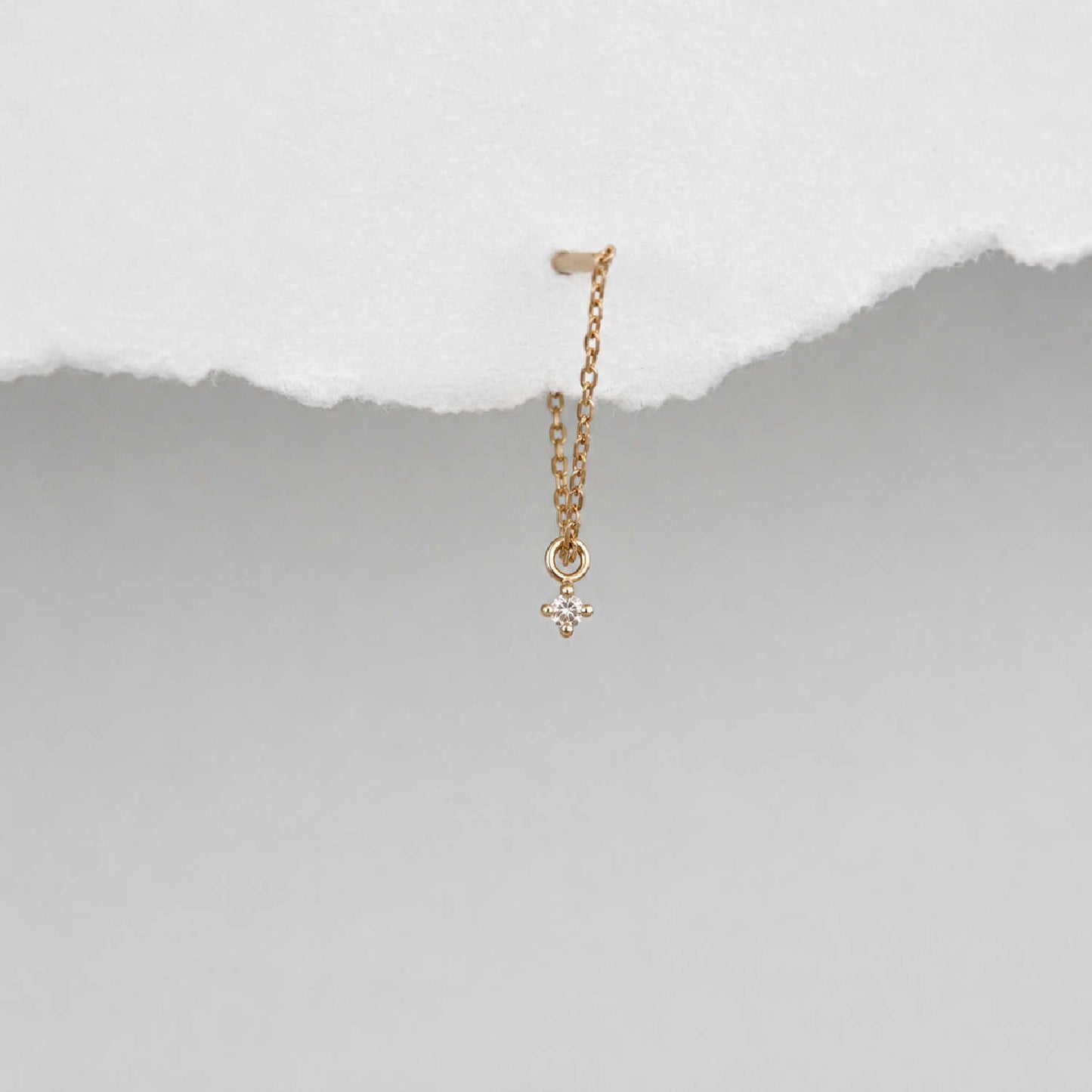 A delicate 14k gold front back chain earring with a floating diamond charm, shown hanging against a textured background