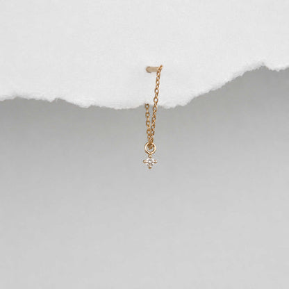 A delicate 14k gold front back chain earring with a floating diamond charm, shown hanging against a textured background
