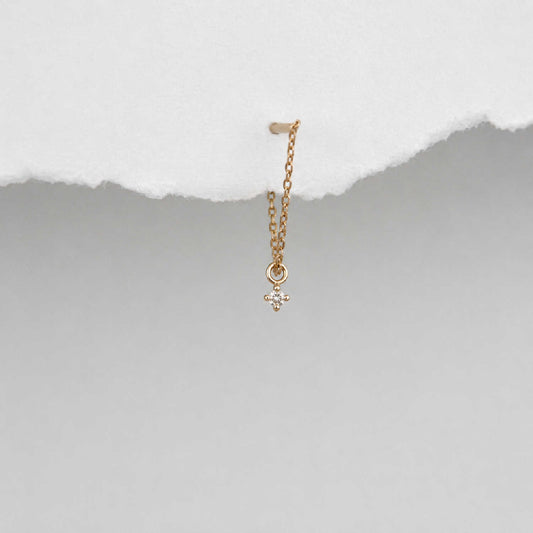 A delicate 14k gold front back chain earring with a floating diamond charm, shown hanging against a textured background