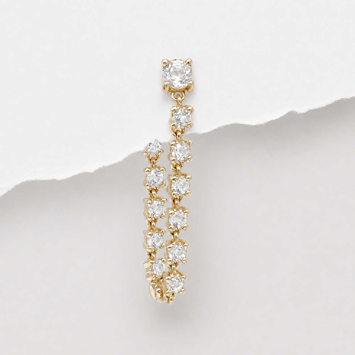 A 14k gold tennis style flat back dangle earring with multiple round-cut diamonds, photographed against a white background with a torn-paper style divider.
