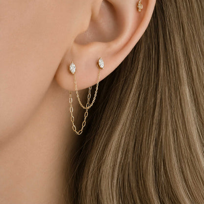 Close-up of a model's ear wearing two 14k gold dangling chain link earring charms across a double piercing with marquise-cut diamond flat back studs.