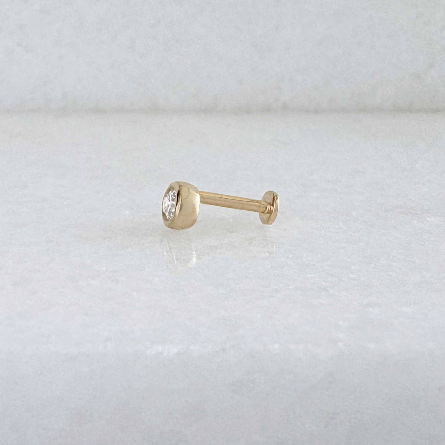 Side view of a single 14k solid gold stud flat back earring with a bezel-set diamond gemstone, shown on a light gray background.