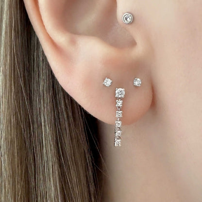 A close-up of a woman's ear wearing a white gold front to back hoop earring with multiple diamonds, along with matching flat back stud earrings