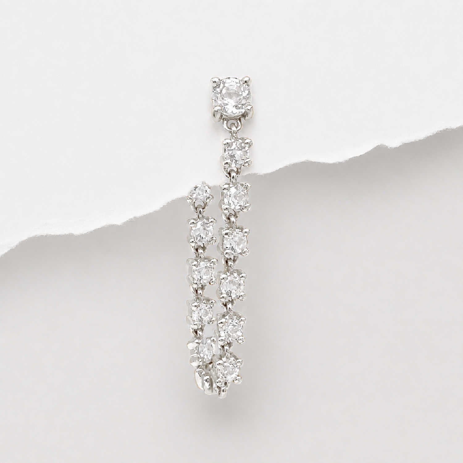 A 14k white gold flat back tennis style dangle earring with multiple round-cut diamonds, photographed against a white background with a torn-paper style divider.