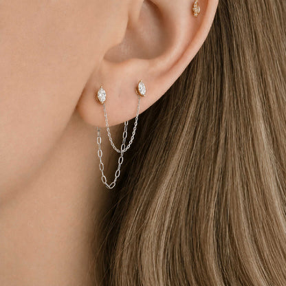 Close-up of a model's ear wearing two 14k white gold dangling chain link earring charms across a double piercing with marquise-cut diamond flat back studs.