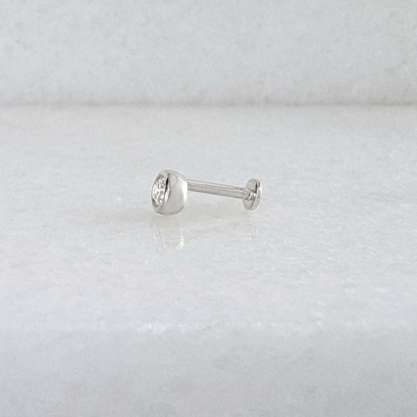 Side view of a single 14k solid white gold stud flat back earring with a bezel-set diamond gemstone, shown on a light gray background.