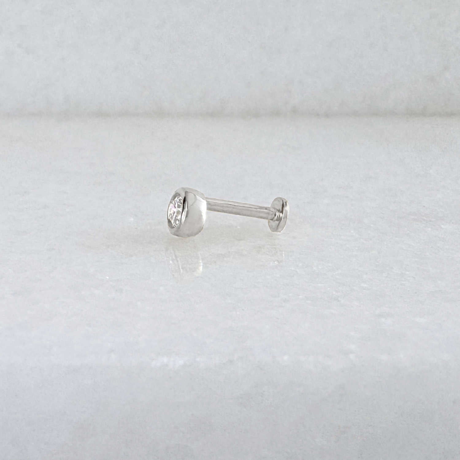 Side view of a single 14k solid white gold stud flat back earring with a bezel-set diamond gemstone, shown on a light gray background.