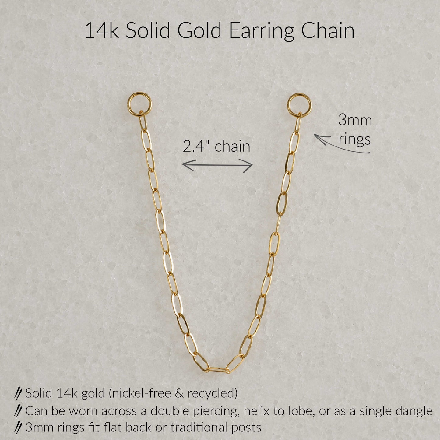 A 14k solid gold earring chain shown on a light gray textured background with text annotations detailing its measurements and features: 2.4-inch chain length, 3mm rings, and product benefits including nickel-free recycled gold and multiple wear styles.