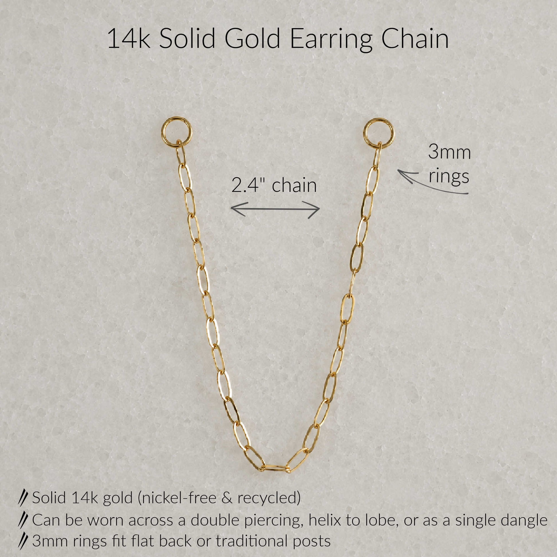 A 14k solid gold earring chain shown on a light gray textured background with text annotations detailing its measurements and features: 2.4-inch chain length, 3mm rings, and product benefits including nickel-free recycled gold and multiple wear styles.