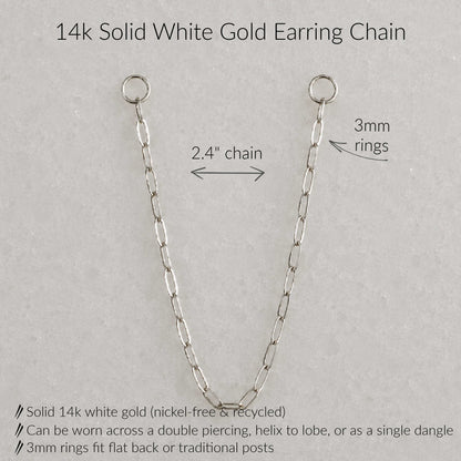 A 14k solid white gold earring chain shown on a light gray textured background with text annotations detailing its measurements and features: 2.4-inch chain length, 3mm rings, and product benefits including nickel-free recycled gold and multiple wear styles.