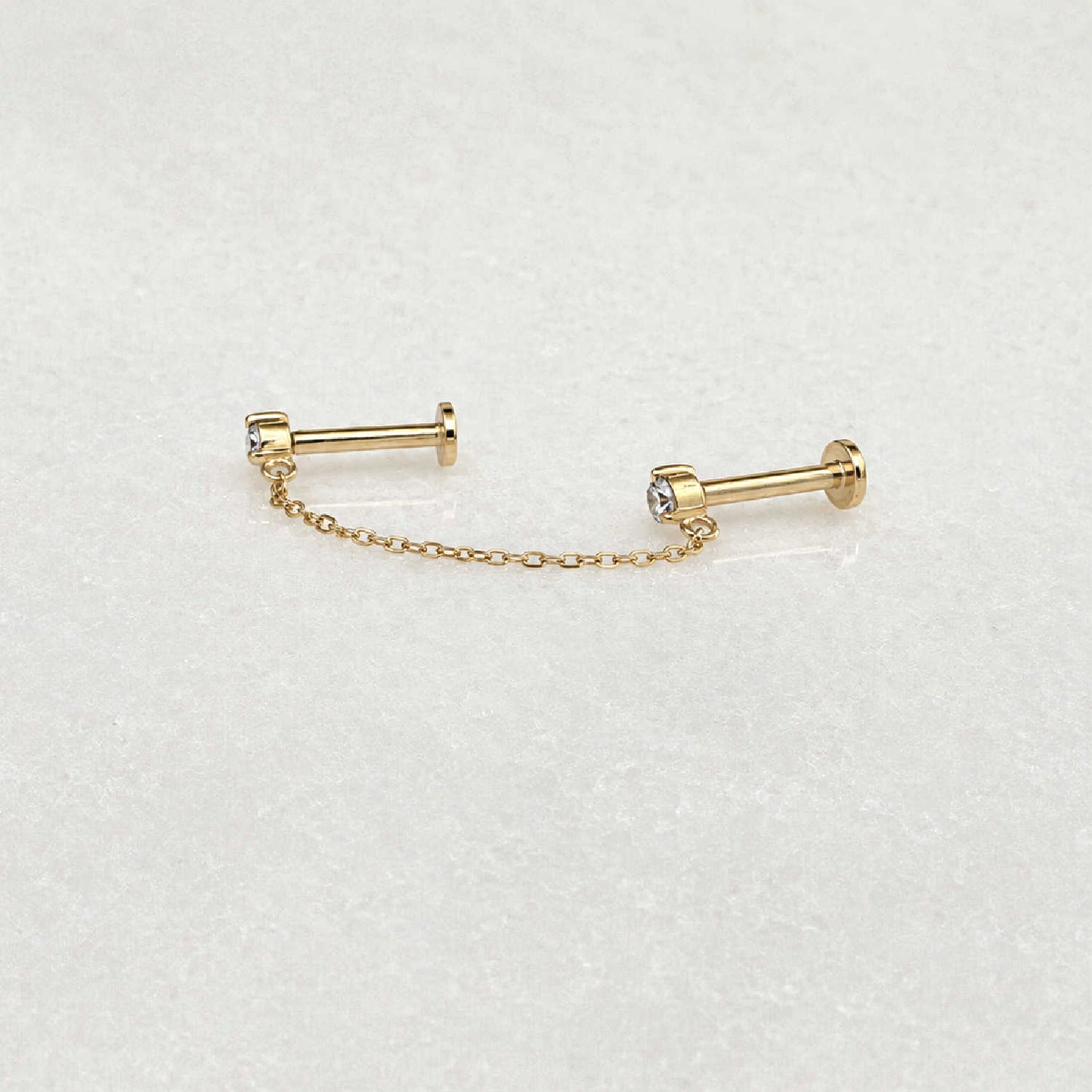 Side view of pair of 14k gold flat back earrings with a short chain connecting the diamond studs