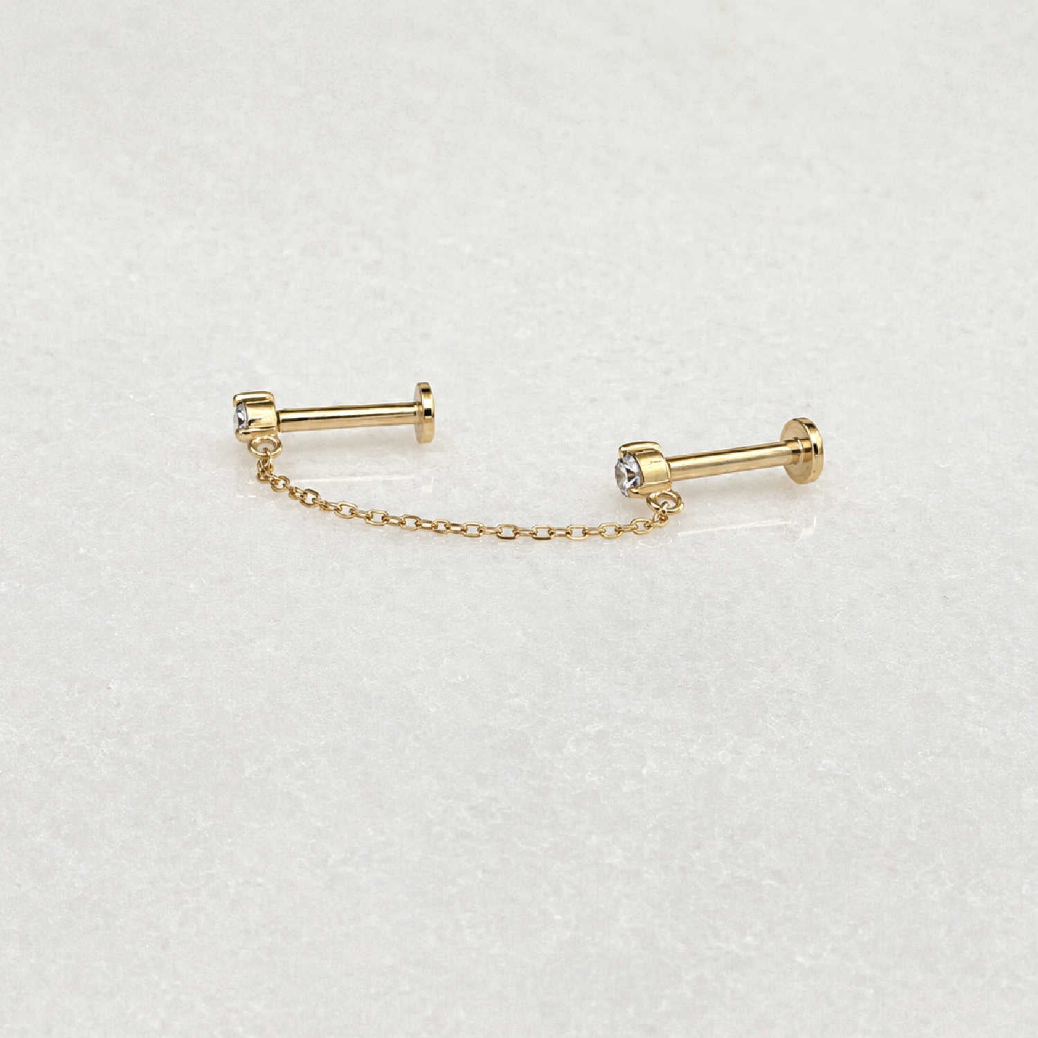 Side view of pair of 14k gold flat back earrings with a short chain connecting the diamond studs