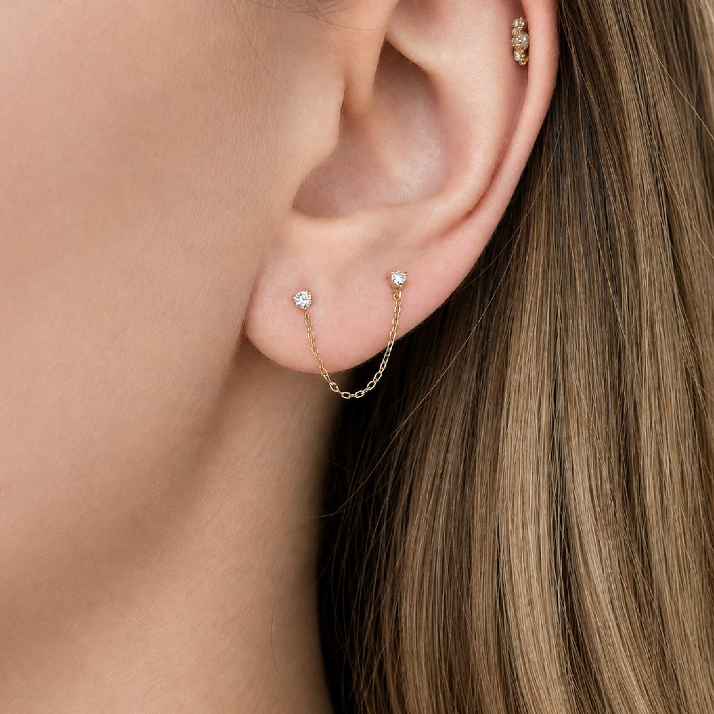 A close-up of a woman's ear wearing a 14k gold chain connected diamond studs