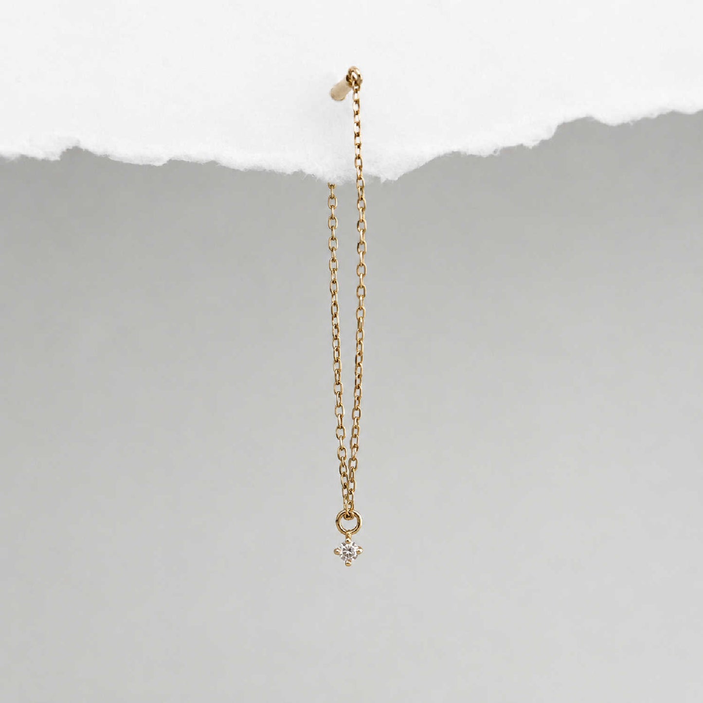 A long delicate 14k gold flat back chain earring with a floating diamond charm, shown hanging against a textured background