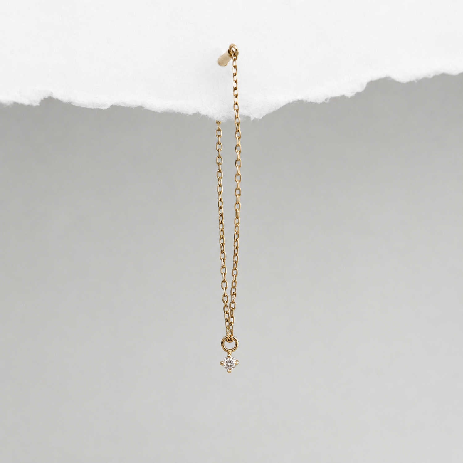 A long delicate 14k gold flat back chain earring with a floating diamond charm, shown hanging against a textured background