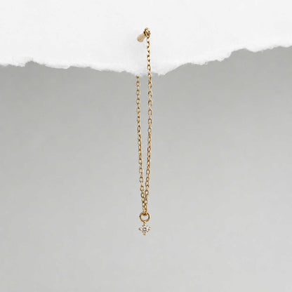 A long delicate 14k gold flat back chain earring with a floating diamond charm, shown hanging against a textured background