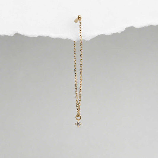 A long delicate 14k gold flat back chain earring with a floating diamond charm, shown hanging against a textured background