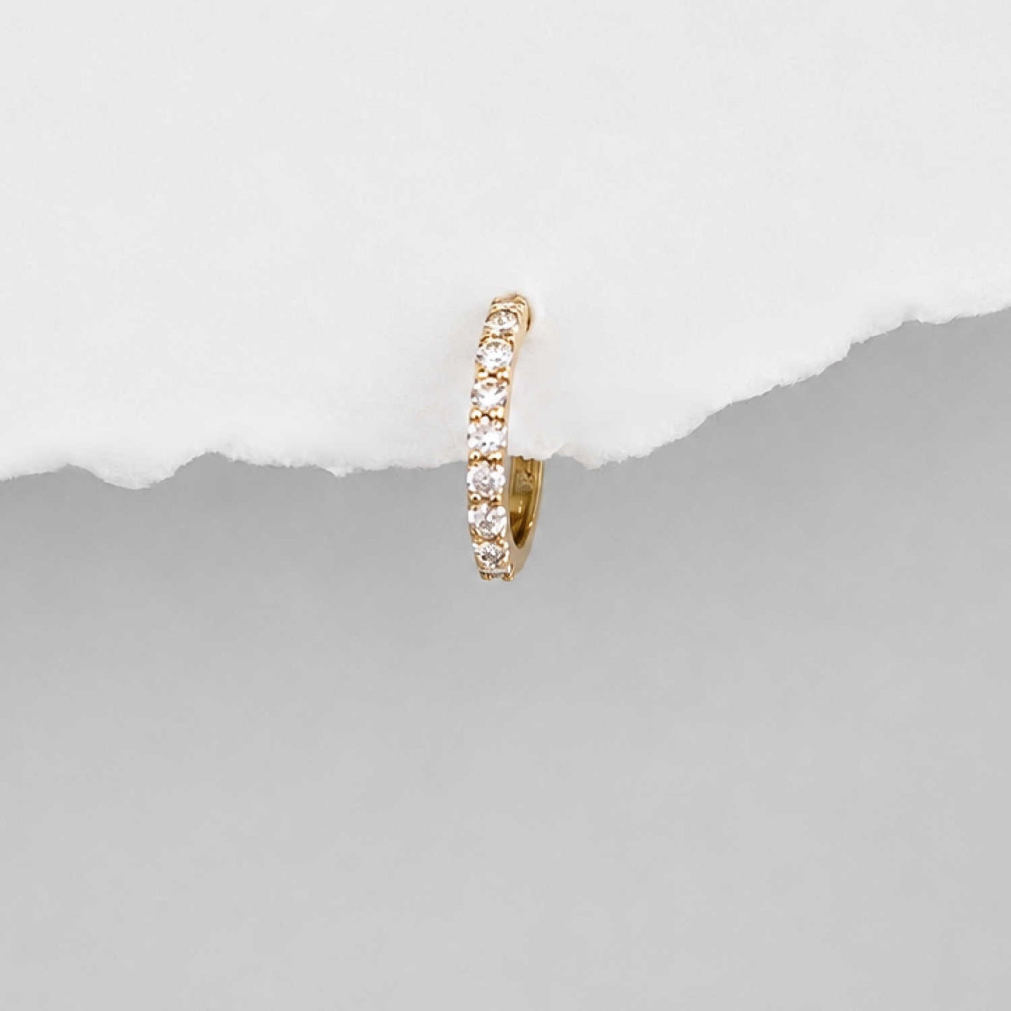 A small 14k gold huggie hoop earring set with diamond gemstones, shown against a split white and gray background.