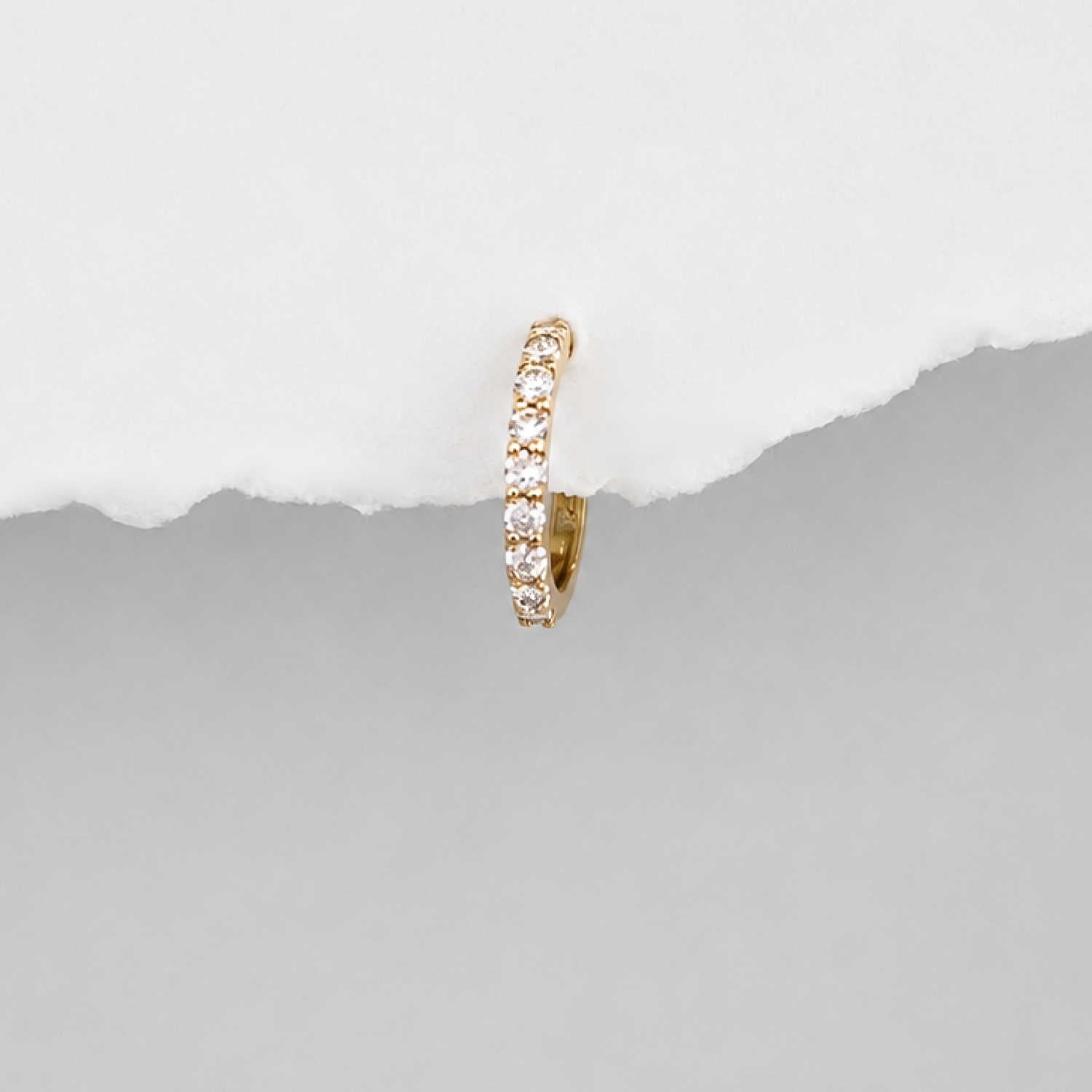 A small 14k gold huggie hoop earring set with diamond gemstones, shown against a split white and gray background.