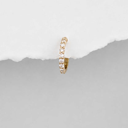 A small 14k gold huggie hoop earring set with diamond gemstones, shown against a split white and gray background.