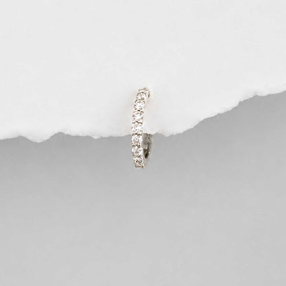 A small 14k white gold huggie hoop earring set with diamond gemstones, shown against a split white and gray background.