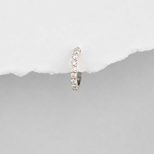 A small 14k white gold huggie hoop earring set with diamond gemstones, shown against a split white and gray background.
