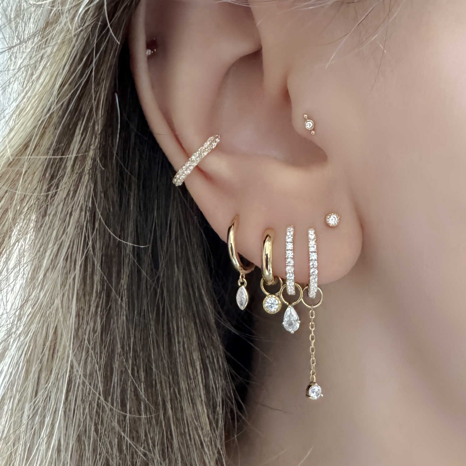 Close-up of a woman's ear with multiple gold hoop earrings, diamond stud earrings, and interchangeable earring charms