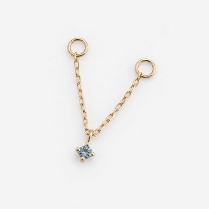 A delicate gold double piercing earring chain charm with two circular loops at the top and a small four-prong blue topaz, shown on a clean white background.