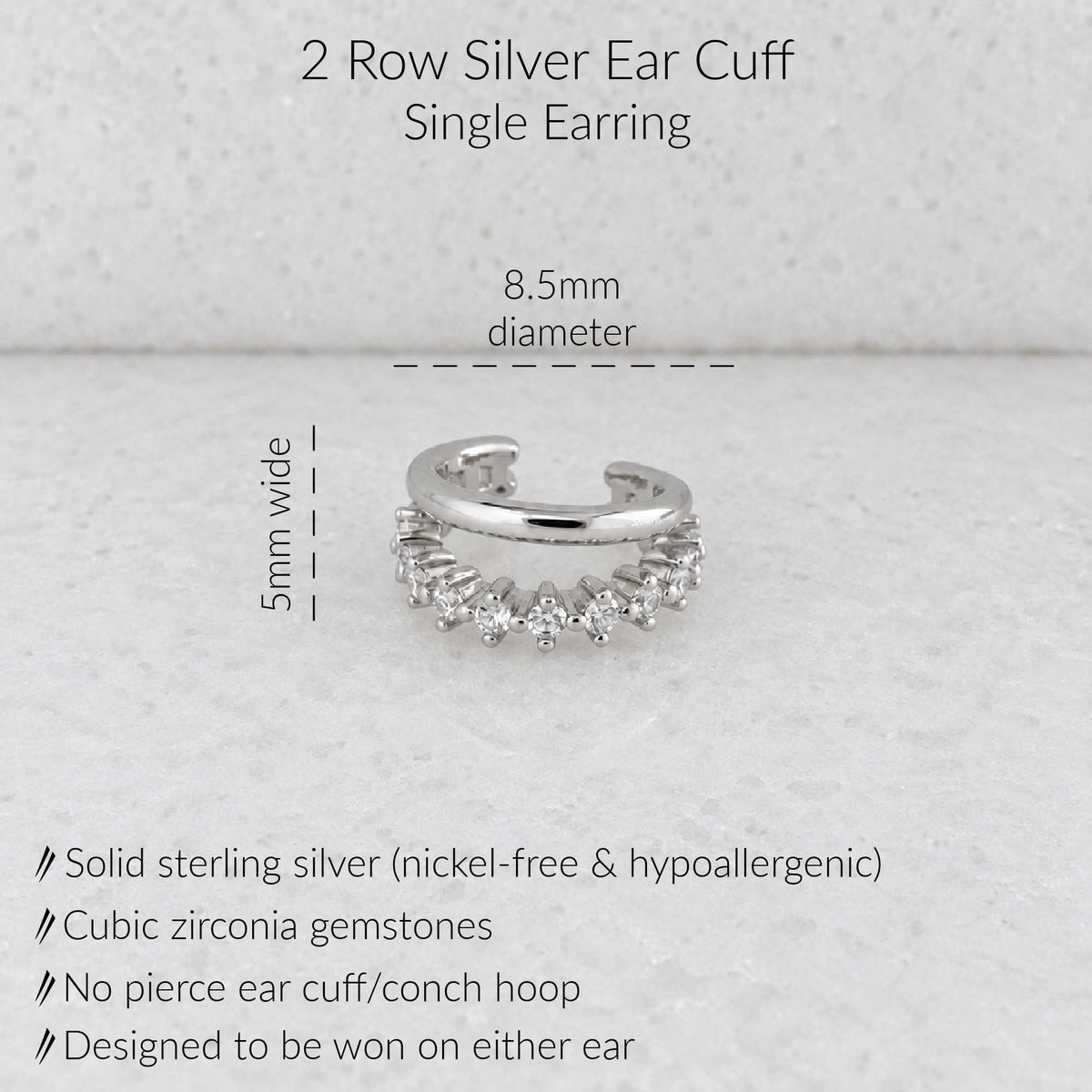A silver open cuff earring with small clear gemstones, shown on a light textured background with text indicating dimensions: 8.5mm diameter and 5mm wide, plus product details about solid sterling silver and cubic zirconia gemstones.