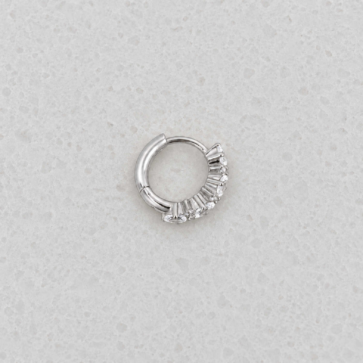 Side view of a sterling silver huggie hoop earring with a vertical cluster of clear oval-cut and round stones.