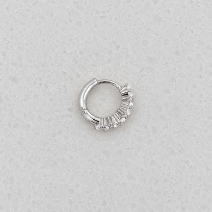 Side view of a sterling silver huggie hoop earring with a vertical cluster of clear oval-cut and round stones.