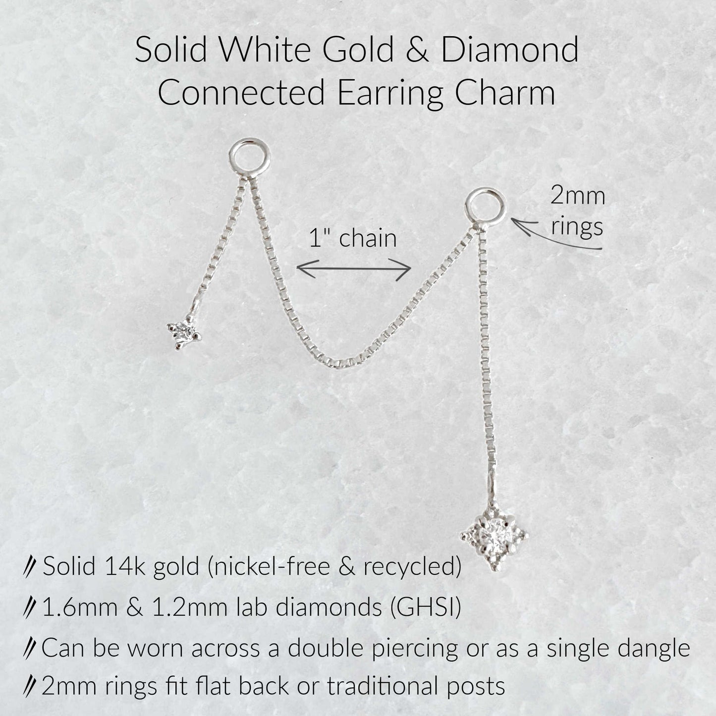 An informational product graphic for a solid white gold and diamond connected earring charm. The image shows a white gold chain with two circular rings, each holding a dangling diamond, with text labels indicating '1" chain', '2mm rings', and product details including 'Solid 14k gold (nickel-free & recycled)'