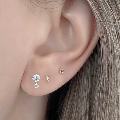 Close up of a woman's ear wearing three styles of 14k gold and diamond earrings, including a 1/2 carat two-stone stud
