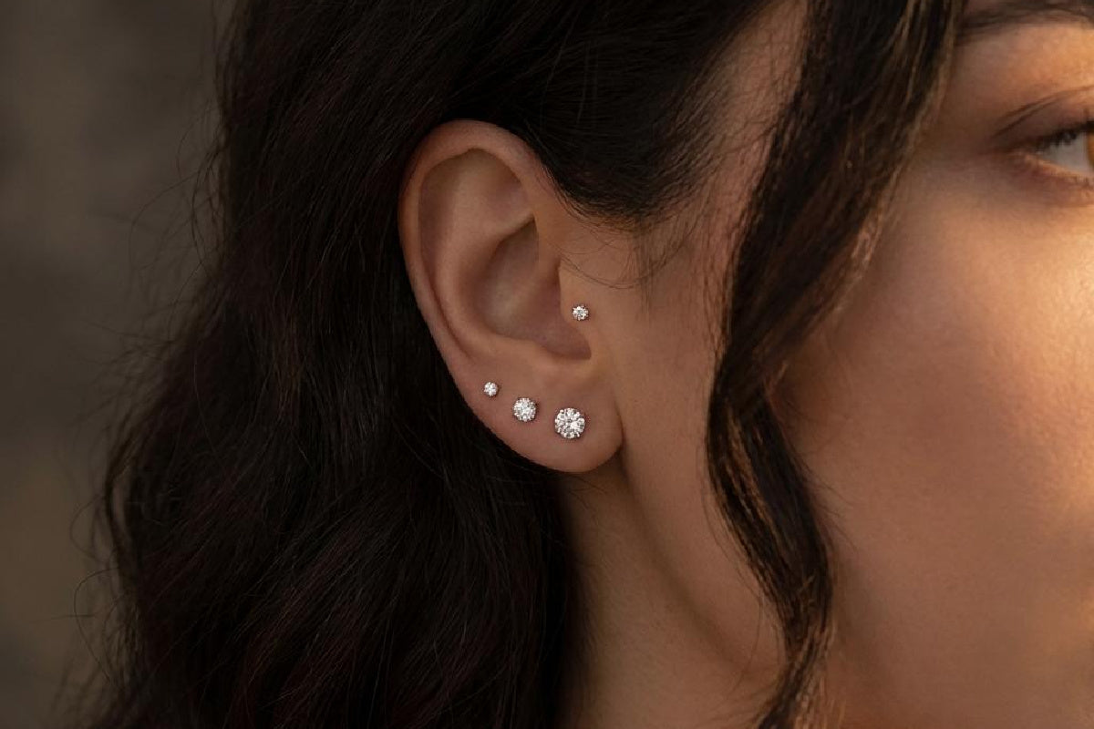 Close-up of a woman's ear with four graduated flat back diamond earrings on a neutral background